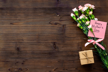 Mother's Day congratulations. Carnations and gift box on dark wooden background top view space for text