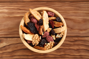 Mix of dried fruit pieces of apple and pear, dried blue plums, strawberries, raspberries, cherries and walnuts in a bamboo bowl on a wooden table. Closeup. Macro