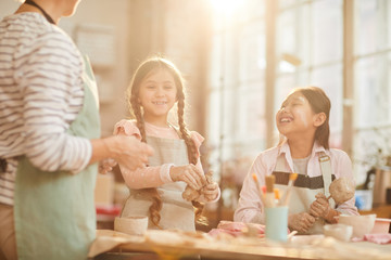 Multi-ethnic group of happy girls creating handmade pottery in art class lit by sunlight, copy space
