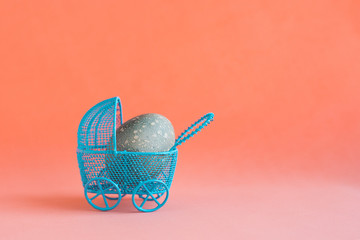 Blue Easter egg in a blue baby carriage on a red coral background