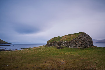 Rural herdsman house in sheep pasture or grazing land made from stones with grass roof from medieval viking age in village Kirkjubour in Streymoy island in Faroe islands, north atlantic ocean in rain.