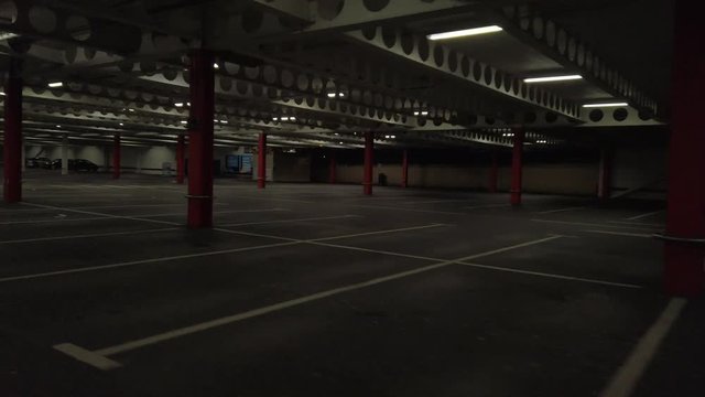 Driving view around empty creepy underground car parking lot basement. Travelling around red pillars structures in partially dark areas.