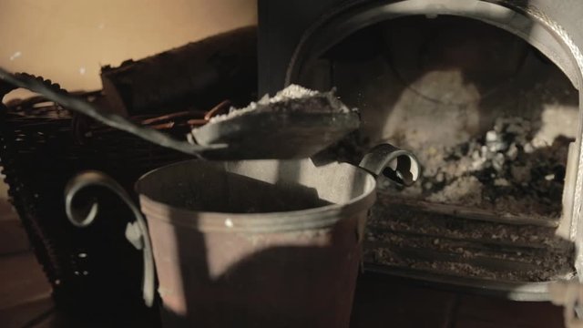 Slow motion close-up of dumping fireplace ashes into a bucket causing a cloud of dust