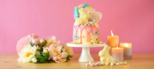 On-trend Easter theme candy land drip cake decorated with lollipops, candy eggs and white chocolate bunny in party table setting.
