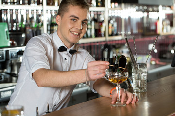 Serving drinks. Positive and smiling bartender mixing drinks.