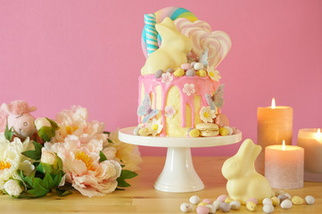 On-trend Easter theme candy land drip cake decorated with lollipops, candy eggs and white chocolate bunny in party table setting.