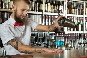 Looking good. Bearded bartender smiling and preparing drink.