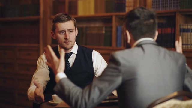 Professors speaking or discuss education in vintage interior. Intelligent elite and education concept. Men with antique bookshelves on background. Intelligent men, scientists spend leisure in library.