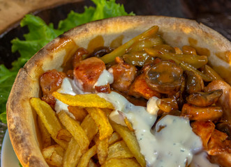 Doner in bread with chicken drumstick, mushrooms, pickles, fries and garlic sauce. Roasted in a stone oven.  Closeup.
