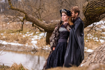 Fototapeta premium Cosplay Ideas. Young Couple Posing as Prince and Princess on Ancient Closing in Spring Forest.