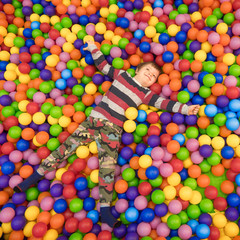 Fototapeta na wymiar Baby boy spending time in the pool filled with balls. Indoor activities. Leisure time for children. Kid plays with colorful plastic balls at entertainment center. Laughter therapy background.