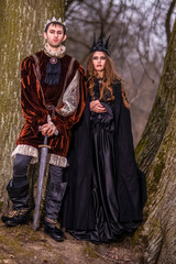 Fototapeta na wymiar Cosplay Ideas.Caucasian Couple as King and Queen in Fur Medieval Outfit With Crowns Posing Together Outdoor.