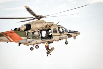 Fotobehang Reddingshelikopter tijdens de vlucht lierende redder © kirill_makarov