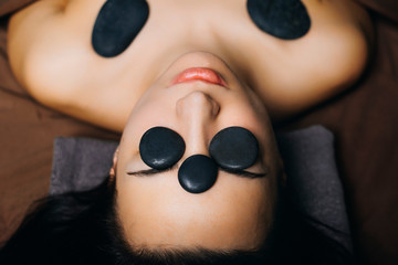 Upper view of adult beautiful female having hot volcanic stones therapy on her face and shoulders...