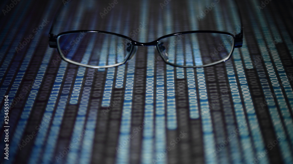 Poster big data analysis. glasses placed on a LED digital panel display white light one and zero binary text number in moving motion pattern. modern technology blue block grid pattern backgrounds