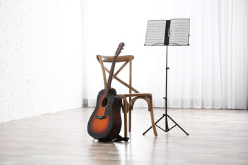 Acoustic guitar, chair and note stand with music sheets indoors