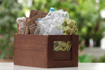 Wooden crate with different garbage on blurred background. Waste recycling concept