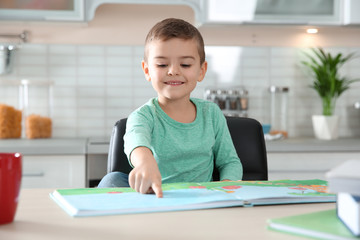 Naklejka premium Cute little boy reading book at table in kitchen