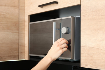Young woman adjusting modern microwave oven in kitchen, closeup