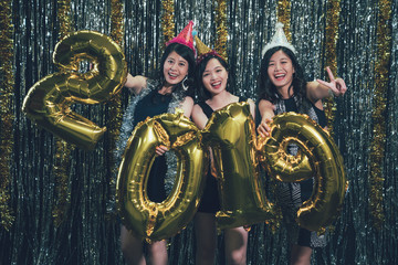 young asian ladies showing victory finger sign face camera smiling. group of charming women carrying colored 2019 number gold balloon countdown new year eve at nightclub cheerfully. night lifestyle.