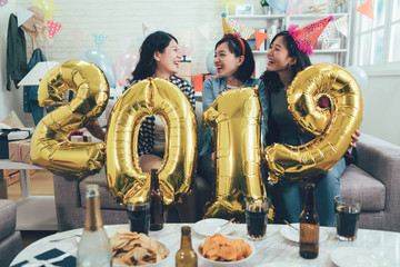 group of best friends carrying 2019 number balloons laughing about funny things sitting on comfortable couch in decorated room at home. countdown new year eve house party start in the daytime.