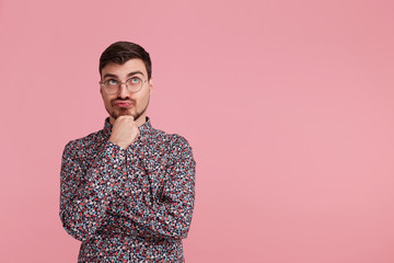 Young man in colorful shirt looking upwards, copy space on the right side,having doubts and with...