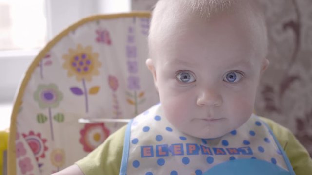 beautiful baby boy at the table take a cookie in his hand, eating it, watching into the camera and babbling close up view slow mo video in 4K