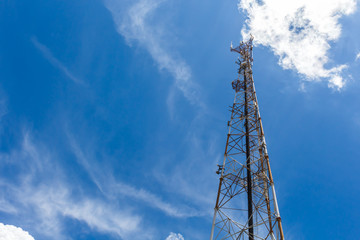 Mobile phone communication repeater antenna tower, with blue sky and white clouds.
