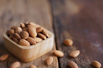 Almond nut in wood bowl on wooden table with green leaf background