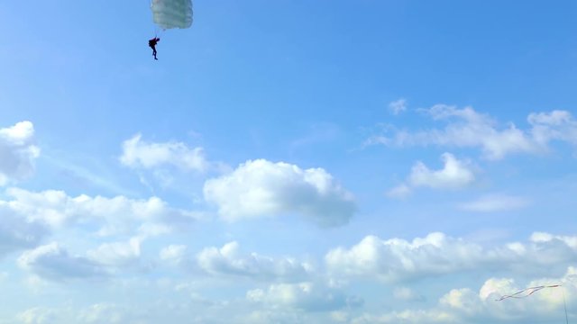Unrecognizable skydiver with parachute flies against the blue sky with white clouds on summer day.