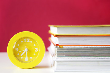 bright yellow plastic alarm clock on the table next to a stack of books on a red background. copy...