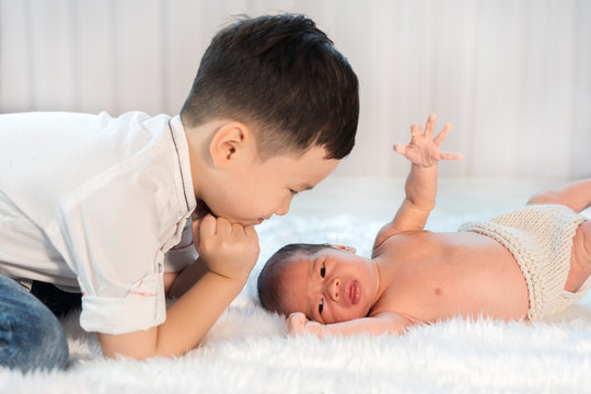 little boy looking his newborn baby brother on bed