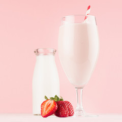 Summer cold fresh dairy cocktail with milk bottle, bright strawberry, straw on white wood board and cute soft pastel pink wall, square.