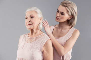 Attentive young blonde girl correcting hairstyle of her old mother