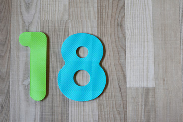 Colorful number eighteen on light brown wooden texture laminate floor background indoors with copy...