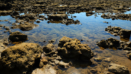 Stone reef beside beach with reflection of summer sky on the sea water.