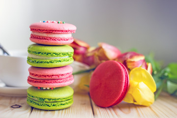 French macaron confectionery in red pink and green colors stand in the form of a turret against the background of tulip flowers. Sweets from almond flour. Birthday background