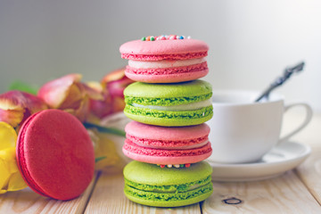 French macaron confectionery in red pink and green colors stand in the form of a turret against the background of tulip flowers. Sweets from almond flour. Birthday background
