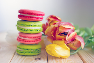 French macaron confectionery in red pink and green colors stand in the form of a turret against the background of tulip flowers. Sweets from almond flour. Birthday background, copy space