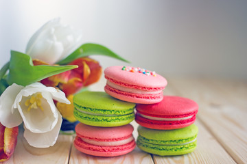 French macarones red, pink and green on a wooden background next to spring flowers. Sweet dessert from France, colorful cookies made from almond flour and egg whites.Confectionery background