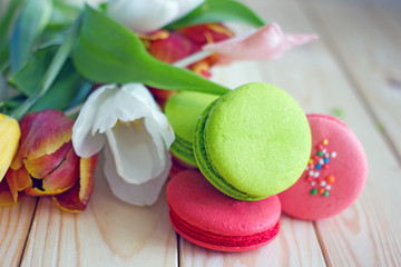French macarones red, pink and green on a wooden background next to spring flowers. Sweet dessert from France, colorful cookies made from almond flour and egg whites.Confectionery background
