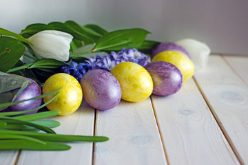 Easter eggs of yellow and lilac color on a wooden background surrounded by greenery, white tulips...