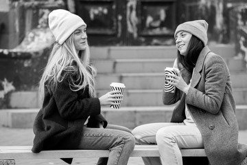 Young girls drinking coffee in city, laughing. Winter weather outdoor. Coffee break. Friends and coffee to go concept. two beautiful long hair girls drinking coffee in the city. 