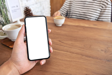 Mockup image of a man's hand holding black mobile phone with blank screen with woman drinking coffee in cafe