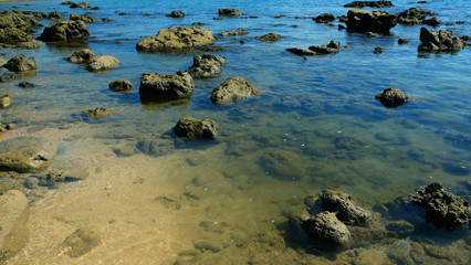 Stone reef beside beach with reflection of summer sky on the sea water.