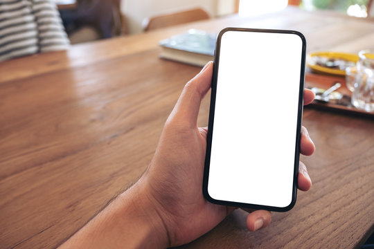 Mockup image of a man's hand holding black mobile phone with blank screen on wooden table