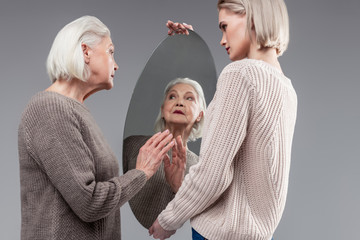 Beaming grey-haired woman touching clean surface of round mirror