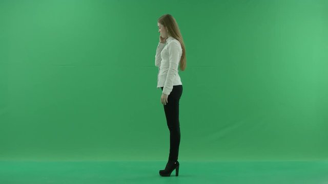 Angry young business woman is talking on mobile phone standing fullength sideways in the centre of a Green Screen