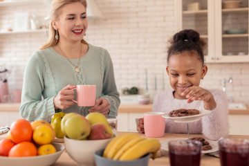 Cheerful cute daughter smiling while looking at sweet cookies