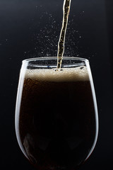 Glass of pouring fizzy drink with ice on a black background